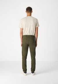 Pantalons extensibles vert olive avec un design ajusté, deux poches arrière, associés à un t-shirt à manches courtes gris clair et des baskets blanches.
