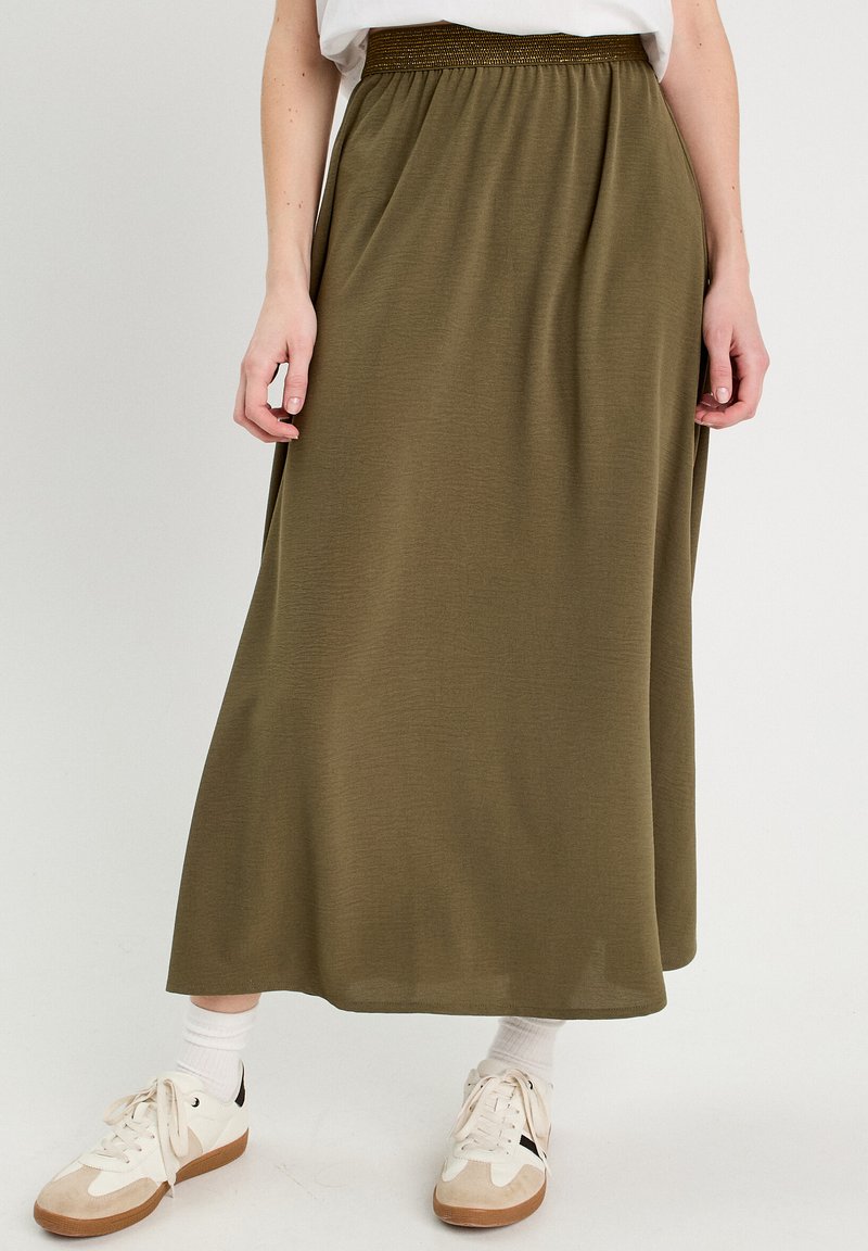 Falda larga color verde oliva con cintura fruncida, confeccionada en una tela suave y fluida, combinada con calcetines blancos y zapatillas.