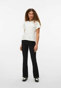 Haut à manches courtes crème avec une coupe décontractée, associé à un pantalon noir évasé et des chaussures noires avec des accents blancs. Texture lisse.