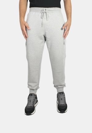 Pantaloni della tuta grigi chiari con vita elasticizzata e cordino, dotati di tasche laterali e polsini affusolati, abbinati a sneakers nere e grigie.