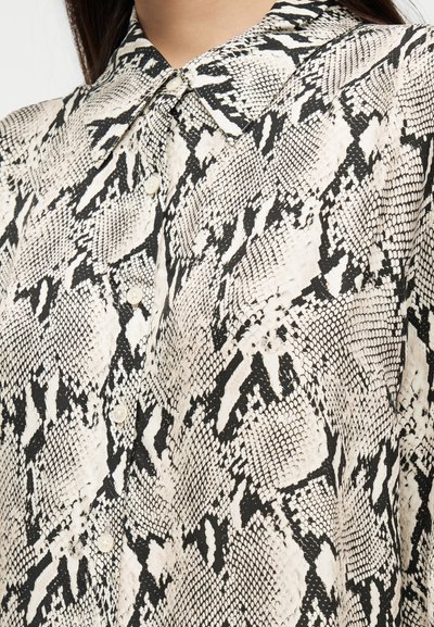 Close-up of a beige and black snake print button-up shirt with a pointed collar worn by a person.