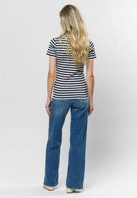 Līniju krekliņš ar īsām piedurknēm tumši zils un balts, kombinēts ar platām zilo džinsu biksēm. Krekliņš ir pieguļošs, bet bikses ir brīvā stilā.