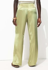 Pantalons wide-leg en satin, vert clair, avec une texture lisse, dotés de poches latérales et d'une fermeture à bouton à l'arrière.