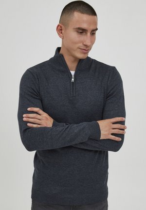 Tamno plavi pulover s polu-zip zatvaranjem, rebrastim manžetama i rubom. Izrađen od mekog pletenog materijala; sadrži mali logo na donjoj strani.