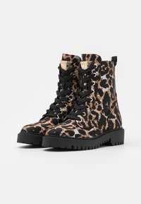 Par de botas de combate con cordones, con un patrón de leopardo en negro, marrón y gris, y suelas de goma negra gruesa, sobre un fondo blanco.