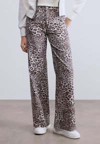 Φαρδιά παντελόνια με λεοπάρ σχέδιο σε μαλακό ύφασμα, με αποχρώσεις του γκρι και του ροζ. Συνδυασμένα με λευκό πουλόβερ και λευκά παπούτσια.