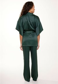 Ensemble deux pièces en satin vert comprenant un top style kimono à manches larges et un pantalon large assorti, texture lisse et ceinture accentuée.