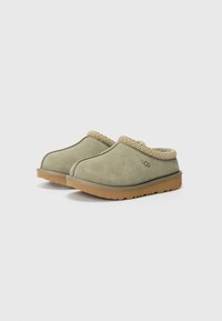 Olivgröna slip-on klackar i mocka med en strukturerad ljusbrun vävd krage och en tan gummisula med ett mönster.