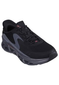 Chaussure de sport noire avec tige en maille, accents gris, semelle épaisse à amortissement et surface texturée pour une meilleure adhérence. Lacets passant par des œillets pour un ajustement sécurisé.