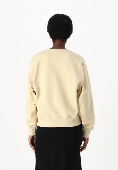 Απαλή μπλούζα σε ανοιχτό μπεζ χρώμα, από μαλακό ύφασμα, με ριμπ μανσέτες και τελείωμα, σε oversized εφαρμογή, πτώσεις στους ώμους και στρογγυλή λαιμόκοψη.