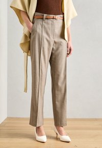 Beige randiga byxor med skräddarsydd passform och bältesöglor, kombinerat med ett bälte i tanfärgad läder. Vita spetsiga klackar kompletterar outfiten.