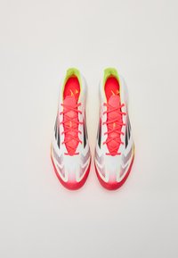White athletic shoes with red and pink accents, lime green collar, and black stripes. Features textured mesh and prominent laces.