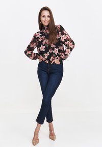 Czarna bluzka w kwiaty z różowymi kwiatami, z długimi bufkami i wysoką szyją; zestawiona z ciemnoniebieskimi skinny jeansami i nagimi szpilkami.