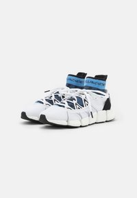 Baskets blanches de sport avec un dessus en tricot extensible, des accents noirs, un col de chaussette bleu et une semelle blanche épaisse et texturée. Présente un design à laçage.