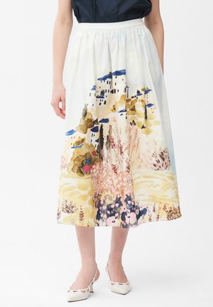 Weißer Midirock mit einem bunten, malerischen Aufdruck von Gebäuden, Blumen und Bäumen, getragen mit weißen High Heels und einer dunklen Bluse.