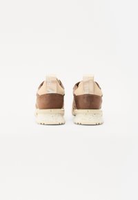 Baskets avec une tige en cuir beige et marron, des accents en textile doux et une semelle texturée. Présente un marquage de la marque sur l'onglet du talon.
