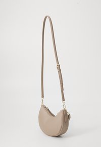 Beige crescent-shaped crossbody bag with adjustable strap and gold-tone hardware, shown against a plain white background.