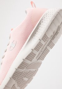 Vaaleanpunainen urheilukenkä, jossa on teksturoitu verkkopinta, harmaat rei'itykset ja valkoinen kumipohja, jossa on uramalli.