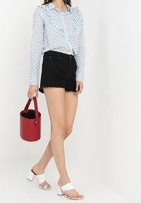 Blusa azul claro con cuello rizado y lunares negros. Pantalones cortos de mezclilla negra con dobladillo deshilachado. Sandalias de tacón bloque blanco y bolso cubo rojo.