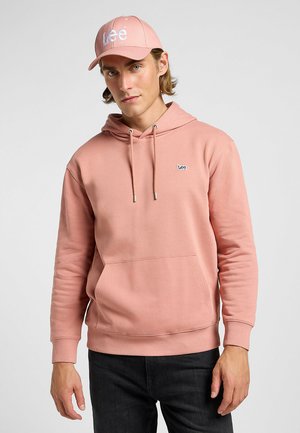 Jasnoróżowy hoodie z kieszenią z przodu i kapturem na sznurku, ozdobiony małym haftowanym logo "Lee". W połączeniu z dopasowaną czapką.