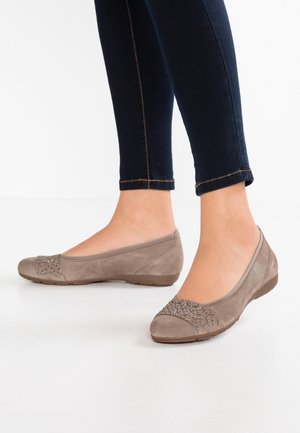 Ballerinasko i taupe ruskind med dekorative nitter på tæerne, båret med mørke skinny jeans mod en hvid baggrund.