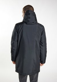Schwarze wasserdichte Jacke mit Kapuze, aus einem glatten Material und mit einem etwas längeren Schnitt. Keine sichtbaren Verschlüsse oder Details auf dem Rücken.