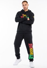 Conjunto de sudadera negra y pantalones deportivos con el colorido logo de Lonsdale; incluye un bolsillo tipo canguro, cintura con cordón y puños acanalados.