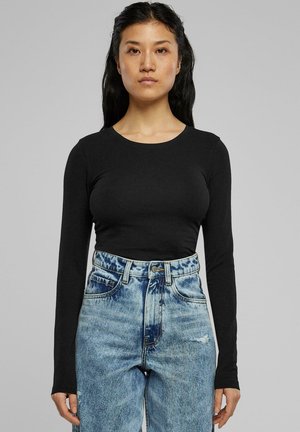 Chemise noire à manches longues en tissu extensible, associée à un jean en denim bleu clair taille haute, avec une finition délavée et des détails usés.