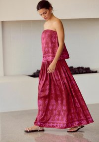 Robe maxi sans bretelles en deux pièces à motifs floraux dans des nuances de rose profond avec des motifs de feuilles. Fabriquée en tissu léger, avec une jupe fluide et plissée.