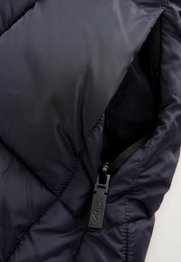 Giacca trapuntata puffer blu navy con finitura testurizzata, dotata di una tasca con zip e un dettaglio in metallo nero con il marchio "Clarks".