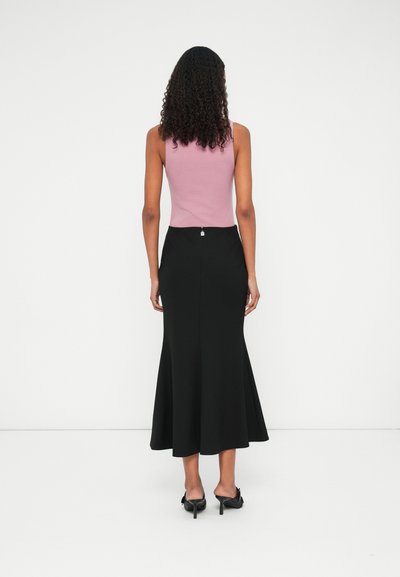 Jupe évasée noire avec une taille ajustée et une fermeture decorative au dos, associée à un haut sans manches rose clair, le tout en tissu lisse.