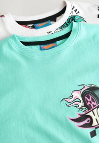 Deux t-shirts superposés, un vert menthe et un blanc. Le t-shirt vert menthe arbore un graphisme audacieux de pneu ; les deux ont des encolures côtelées.