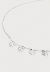 Ασημένιο κολιέ με αλυσίδα που διαθέτει πέντε κρεμαστά σε σχήμα καρδιάς· δύο με διακοσμητικά στρας, τρία με λείες μεταλλικές επιφάνειες.