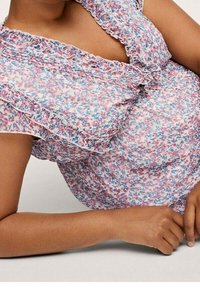 Kukka-aiheinen paita röyhelöhihoilla, jossa on vaaleanpunaisia, sinisiä ja valkoisia kuvioita. Kevyt kangas rentoa istuvuutta varten, kerätty yksityiskohta kaula-aukossa.