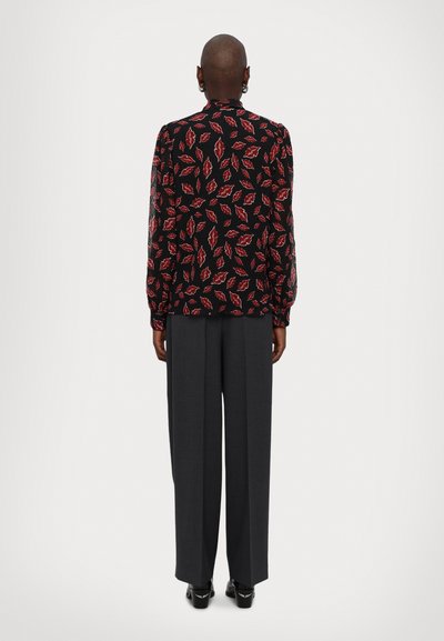 Blouse noire avec motif de feuilles rouges, manches longues, poignets froncés, associée à un pantalon gris taille haute, complété par des chaussures à talons noires.
