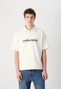 Kremena polo majica s kratkim rukavima, s plavim "calvin klein" logotipom i natpisom. Mekani materijal s klasičnim dizajnom ovratnika.