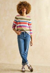 Striped long-sleeve shirt in pastel colors, paired with high-waisted blue jeans, rolled cuffs, gray flats, and patterned socks.
