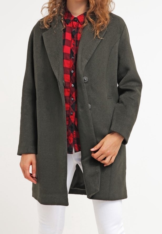 Manteau long vert olive, design structuré, deux boutons, poches latérales. Associé à une chemise à carreaux rouge et noir et un jean blanc.