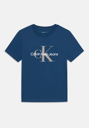 Temno modra bombažna majica s krožnim izrezom. Ima velik beli in bež Calvin Klein logo, printan na sprednji strani.