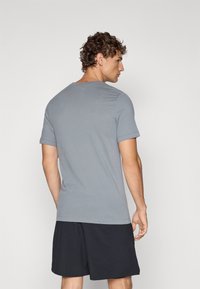 Grå t-skjorte med korte ermer og rund hals, laget av mykt stoff, kombinert med svarte shorts. Glatt tekstur, tettsittende design.