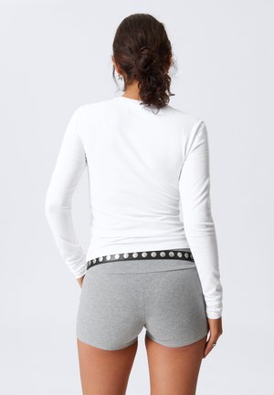Long-sleeve white top with fitted silhouette paired with gray shorts featuring a black waistband adorned with silver studs.