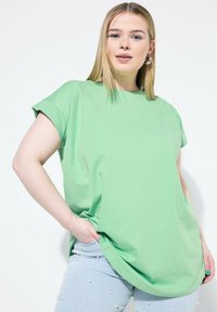 Světle zelené oversized tričko z bavlny s krátkými zkrácenými rukávy, se zaobleným spodním lemem a uvolněným střihem. Nohavice jsou doplněny o ozdobené džíny.