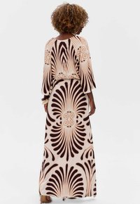 Vestido maxi con un diseño fluido, tela ligera y un fondo beige con patrones intrincados en espiral de color marrón oscuro y mangas anchas.