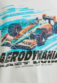 Tricou alb cu un grafism colorat al unei mașini de curse, cu accente albastre și portocalii, înconjurată de linii dinamice și text îndrăzneț.