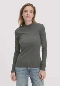 Olivgrünes, geripptes Langarmpoloshirt mit schmalem Schnitt, weicher Textur und minimalen Nähten, kombiniert mit hellblauen Jeans.