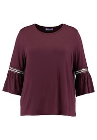 Burgundinpunainen yläosa, joka on valmistettu pehmeästä kankaasta. Siinä on pyöreä pääntie ja kolme neljäsosaa pitkät liehukkeelliset hihat, joissa on koristeelliset pitsiosuudet.