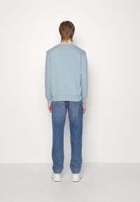 Ljusblå sweatshirt med rund hals och ribbade ärmar, tillsammans med urblekta denimjeans. Jeansen har en rak benform och slitna detaljer.