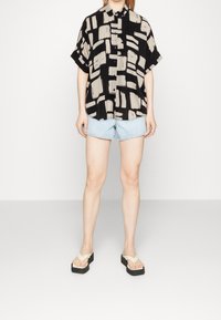 Czarna i beżowa koszula krótki rękaw w wzory z zapięciem na guziki, zestawiona z jasnymi szortami dżinsowymi i klapkami na platformie.