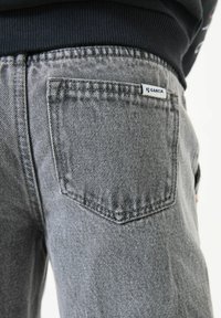 Jeans in denim grigio con una tasca posteriore dotata di un'etichetta bianca con la scritta "GARCÍA". Il tessuto presenta una finitura testurizzata e un design classico.