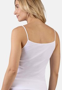 Woman with blonde hair wearing a white sleeveless top, shown from the back and turning head to the left with a slight smile.